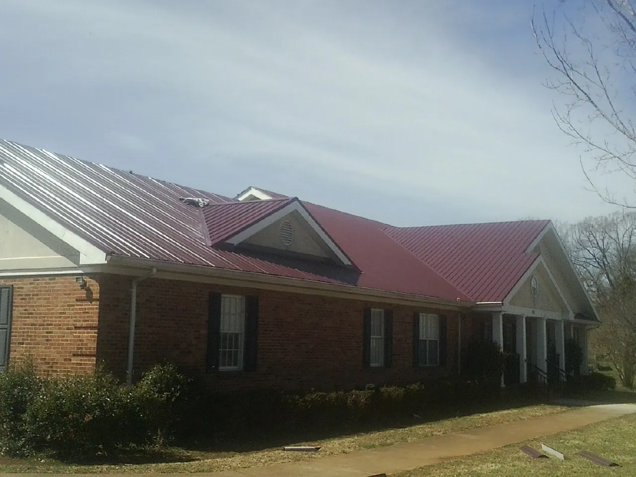 Red metal roof with gabled entries on a long brick building, from a Hail Damage Roof Repair job in Salinas