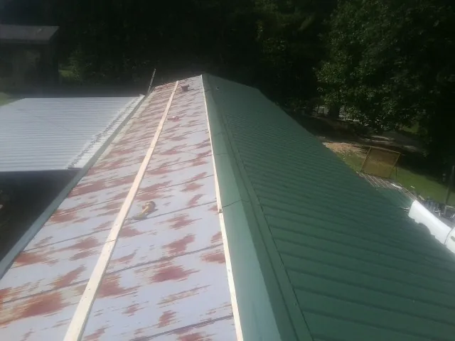 Old rusted panels beside newly installed green metal roofing — Wind Damage Roof Repair by Roofing Brothers in Salinas