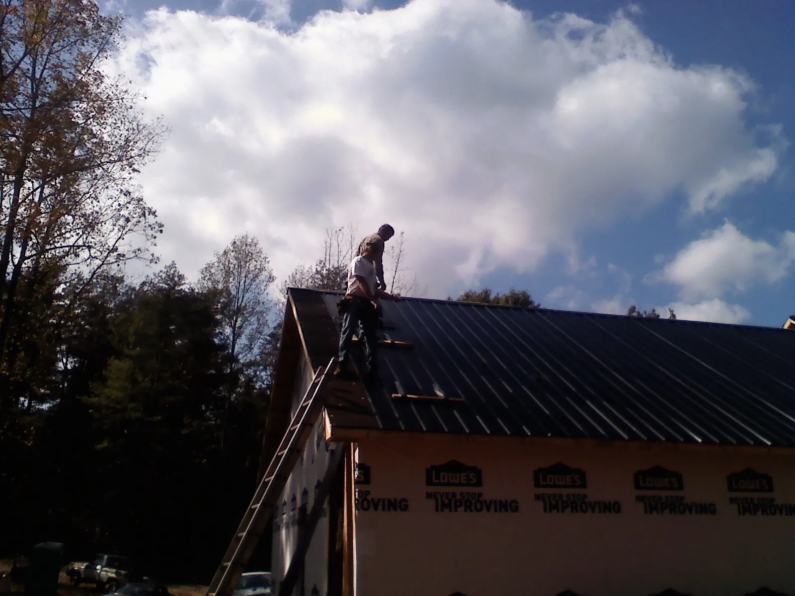 Roofer fastening dark metal panels high against a cloudy sky, from a Roof Inspection job in Salinas