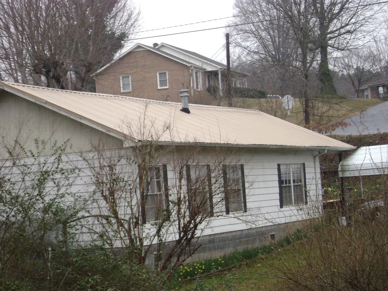 Tan metal roof on a white sided house set into a hillside — Commercial Roofing by Roofing Brothers in Salinas